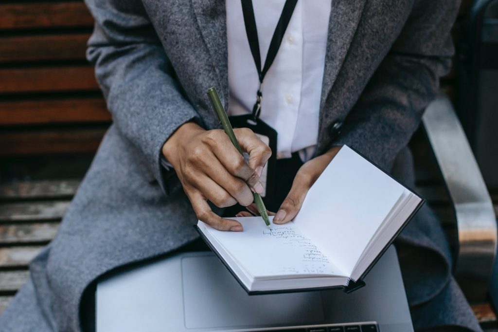 crop unrecognizable woman writing thoughts in notebook while sitting on bench