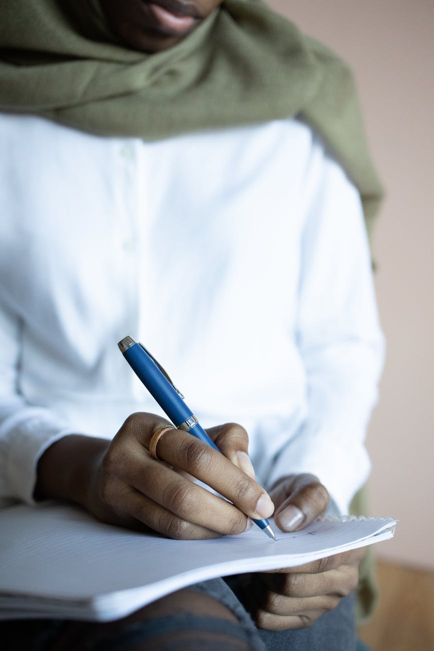 crop black muslim woman writing in copybook