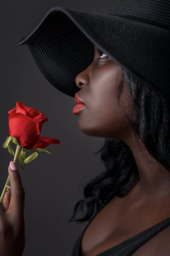 a woman wearing a hat holding a red rose