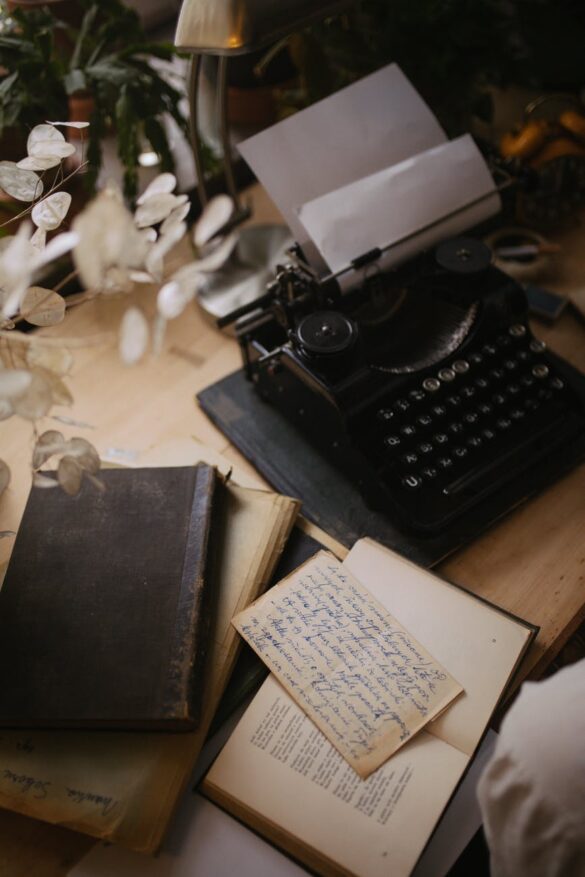 a black typewriter with a bond paper beside a book on a wooden table